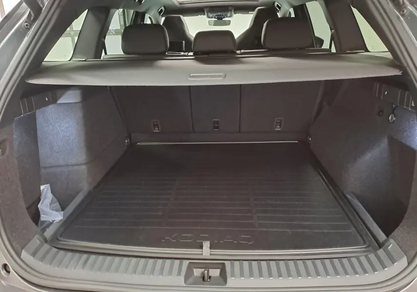 Coffre ouvert vu de l'arrière du Skoda Kodiaq gris graphite, avec tapis de coffre marqué KODIAQ et cache-bagages déployé.