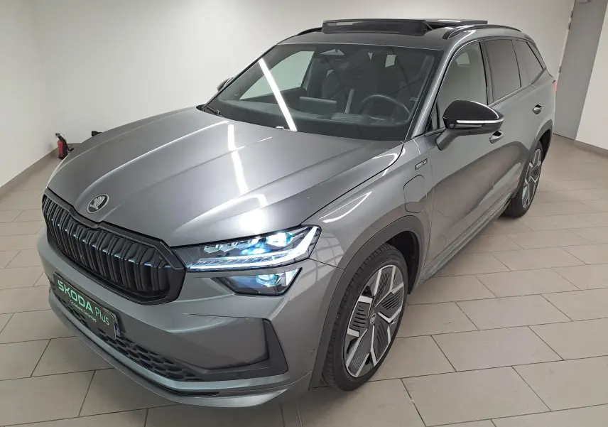 Vue 3/4 avant droite du Skoda Kodiaq gris graphite avec phares allumés et toit panoramique ouvrant visible.