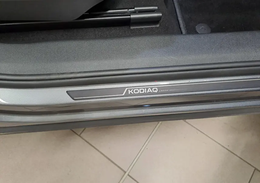 Gros plan sur la plaque de seuil de porte "KODIAQ" du SUV Skoda gris graphite, intérieur avec moquette noire visible.