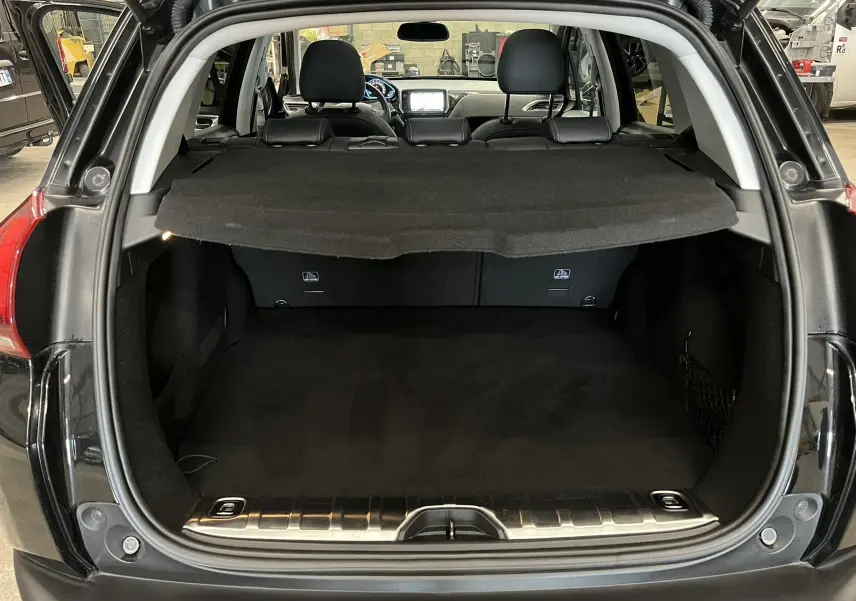 Coffre ouvert vu de l'arrière d'un Peugeot 2008 noir, avec cache-bagages et intérieur sombre visible.