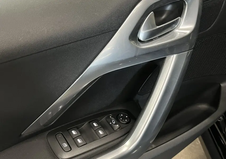 Gros plan sur la poignée intérieure et les commandes de vitres côté gauche d’une Peugeot 2008 noire de 2018.