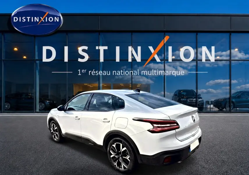 Vue 3/4 arrière droite d'une Citroën C4 X blanche avec feux arrière LED et jantes alliage noires devant un showroom Distinxion.