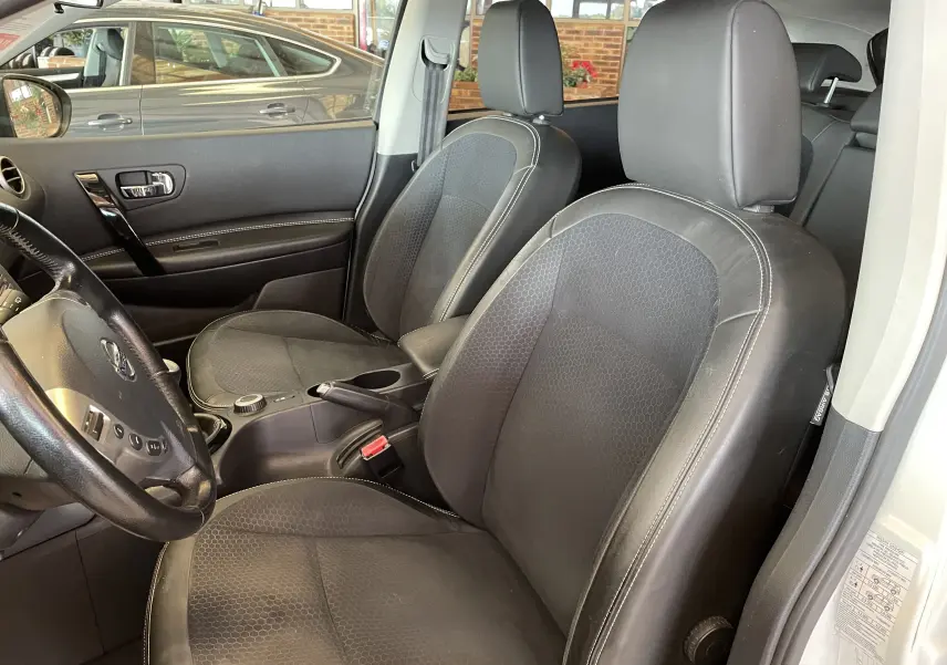 Vue intérieure côté conducteur du Nissan Qashqai blanc 2013, sièges noirs en tissu et cuir avec volant multifonction.