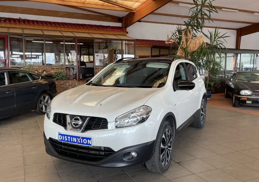 Vue 3/4 avant d'un Nissan Qashqai blanc 2013 avec toit noir et jantes alliage noires en showroom.