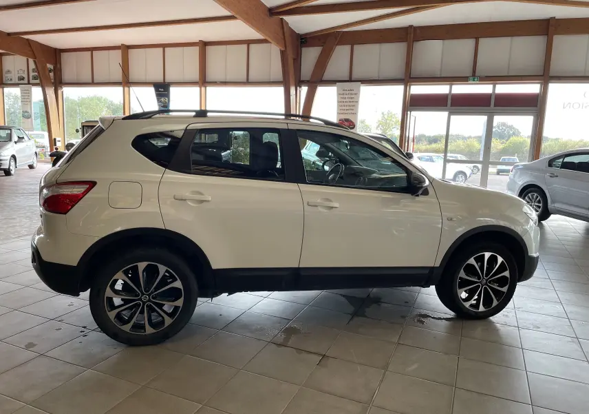 Profil côté gauche d'un Nissan Qashqai blanc 2013 en intérieur, avec jantes alliage noires et toit ouvrant.