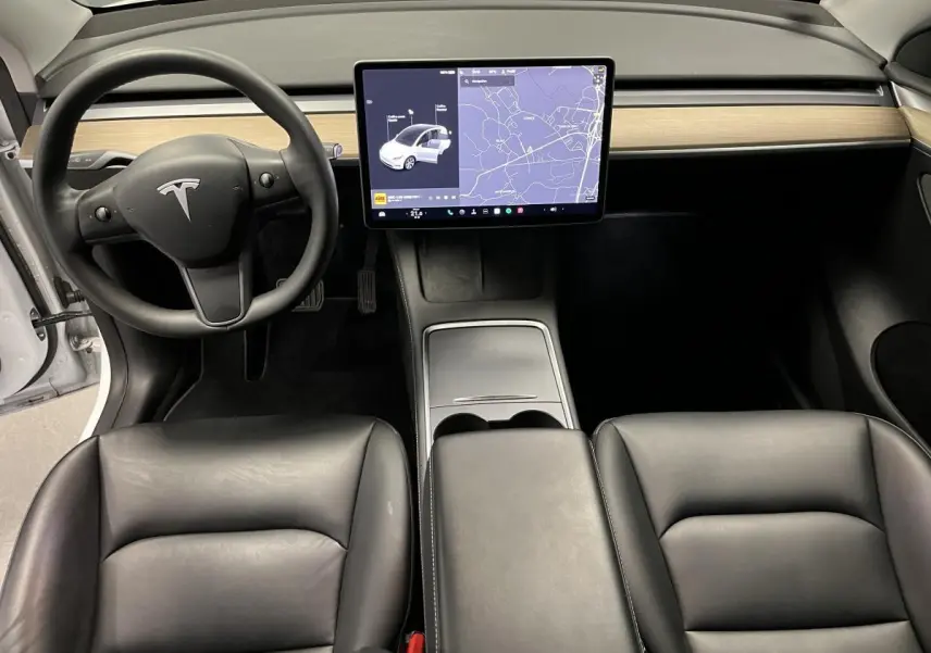 Vue intérieure avant de la Tesla Model Y blanche avec tableau de bord minimaliste et écran tactile central affichant la navigation.