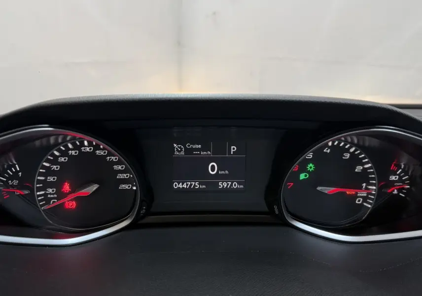 Tableau de bord de Peugeot 308 noir, affichage digital au centre avec compteurs analogiques et témoins lumineux allumés.