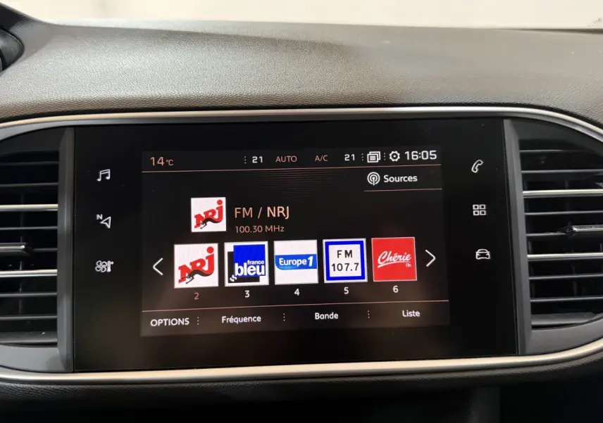 Écran tactile central allumé affichant les stations radio dans l’habitacle d’une Peugeot 308 noire.
