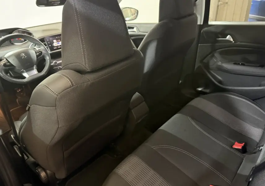 Vue intérieure arrière côté droit de la Peugeot 308 noire, montrant les sièges tissu et le tableau de bord avant.