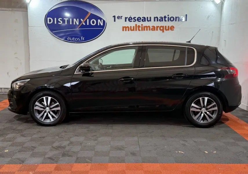 Profil côté gauche d'une Peugeot 308 noire Puretech 130 Allure 2020 dans un showroom avec logo Distinxion en arrière-plan.