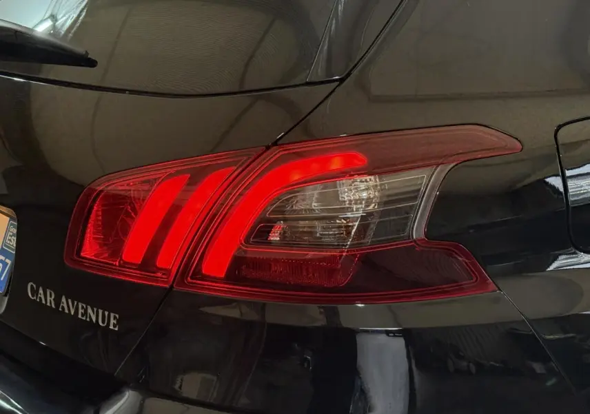 Gros plan sur le feu arrière droit rouge d’une Peugeot 308 noire, avec reflet de l’environnement intérieur visible.