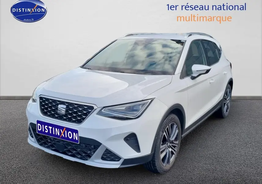 Vue 3/4 avant droite d'un SEAT Arona blanc 2023 avec jantes alu et barres de toit visibles.