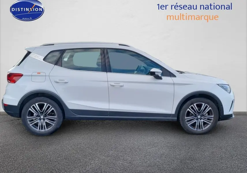 Vue de profil côté gauche d'un SEAT Arona blanc 2023 avec jantes alliage et barres de toit noires.