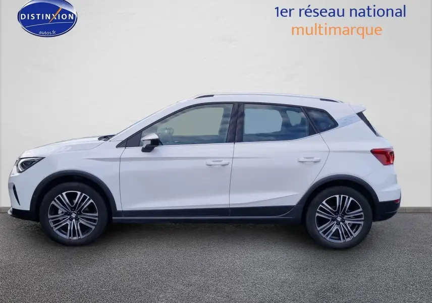 Vue latérale gauche d'un SEAT Arona blanc 2023 avec jantes alliage et barres de toit noires.