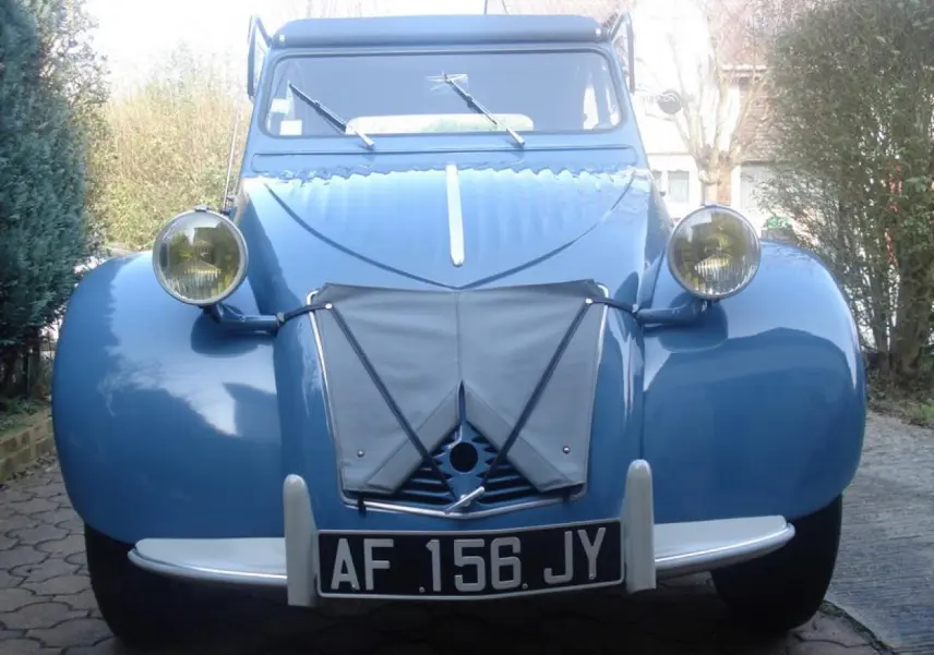 Vue avant d'une Citroën 2 CV bleu clair de 1960 avec ses phares ronds jaunes et sa plaque d'immatriculation noire.