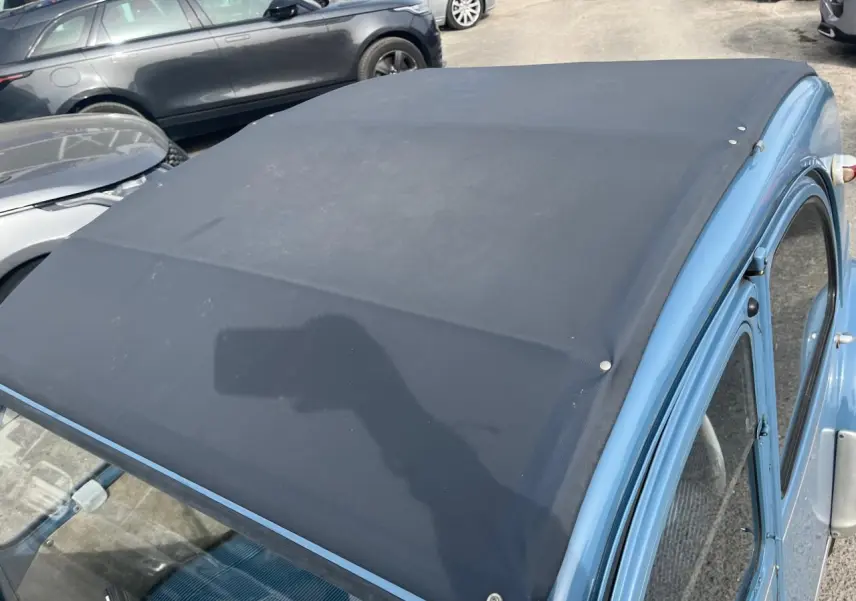 Vue 3/4 avant droit d'une Citroën 2CV bleu clair de 1960 avec toit en toile noir relevé.