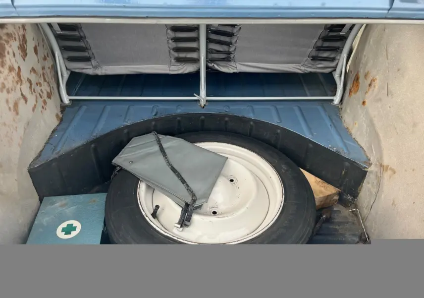 Vue intérieure du coffre d'une Citroën 2 CV bleu clair de 1960, avec roue de secours et trousse à outils grise.