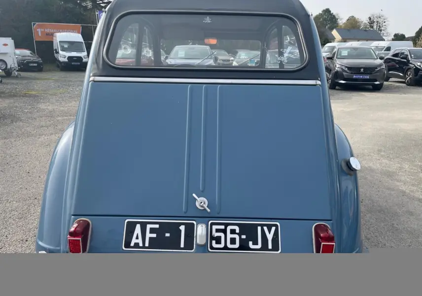 Vue arrière d'une Citroën 2 CV bleu clair de 1960, avec capote noire et plaques d'immatriculation noires.