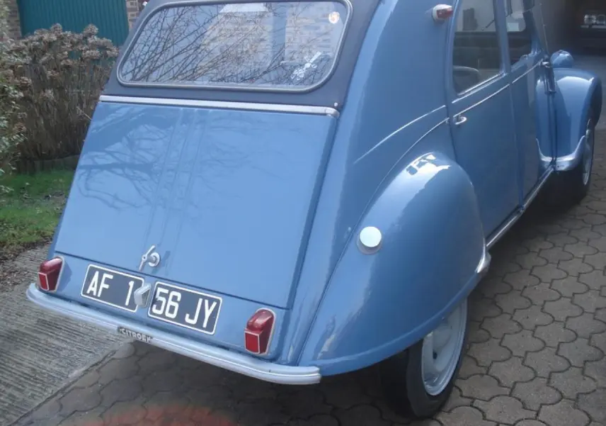 Vue 3/4 arrière droite d'une Citroën 2CV bleu clair de 1960 avec plaques noires et feux arrière rectangulaires rouges.