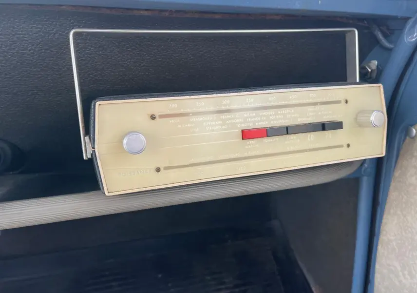 Gros plan sur la radio vintage beige du tableau de bord bleu clair d'une Citroën 2CV de 1960.
