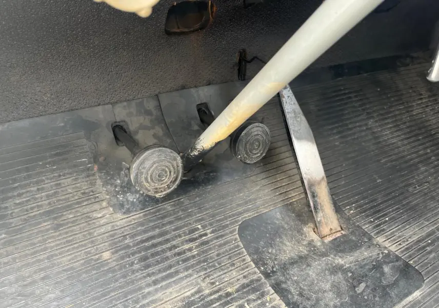 Gros plan sur les pédales et le levier de vitesse gris d'une Citroën 2 CV bleu clair de 1960, intérieur usé et poussiéreux.