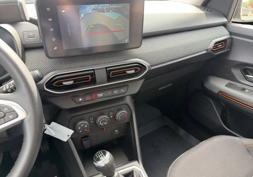 Vue intérieure côté passager de la planche de bord noire avec écran tactile et levier de vitesses manuel de la Dacia Sandero Stepway blanche.