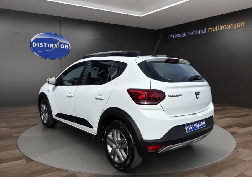 Vue 3/4 arrière droite d'une Dacia Sandero Stepway blanche avec barres de toit et jantes alliage en showroom.