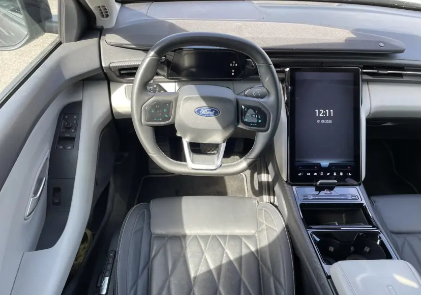 Vue intérieure frontale du Ford Explorer 2025 gris, avec volant multifonction et grand écran tactile vertical central.