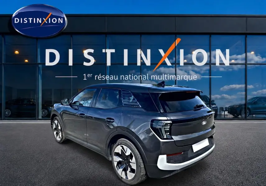 Vue 3/4 arrière droite du Ford Explorer électrique gris, avec jantes alu et vitres arrière surteintées, devant une vitrine Distinxion.