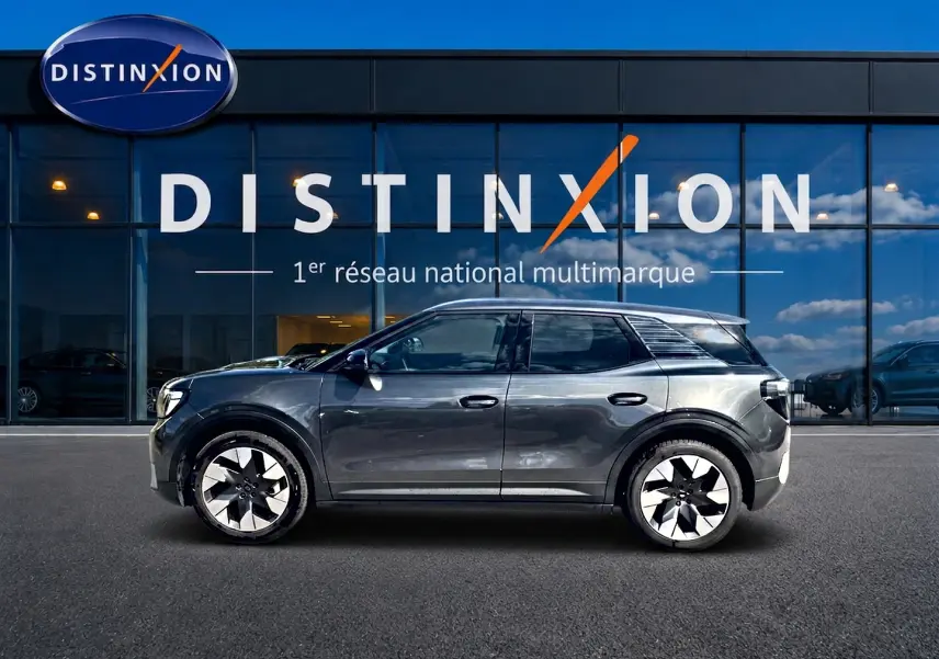 Vue latérale droite d'un Ford Explorer électrique gris métallisé 2025, avec jantes alu et vitres surteintées, devant une vitrine Distinxion.