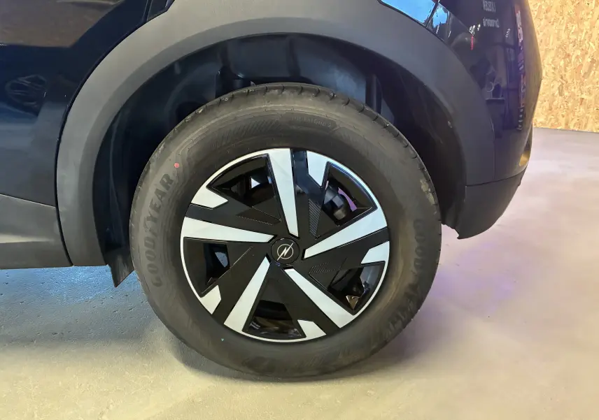Gros plan sur la roue arrière droite noire d’un Opel Mokka 1.2 Turbo Hybrid 136 Edition avec jante au design géométrique bicolore.