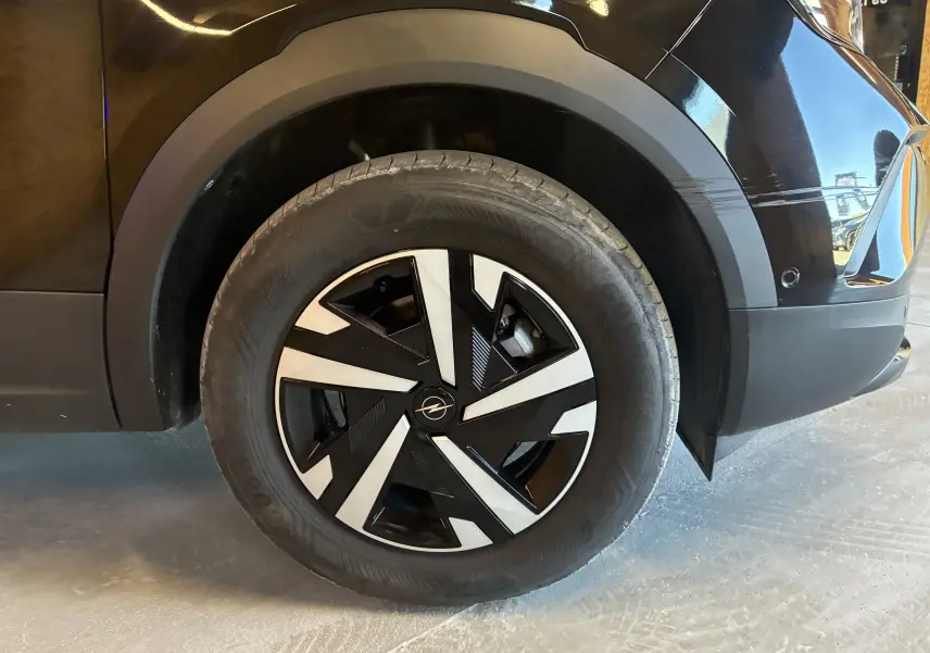 Gros plan sur la roue avant droite noire d’un Opel Mokka 1.2 Turbo Hybrid 136 Edition avec jante au design géométrique bicolore.