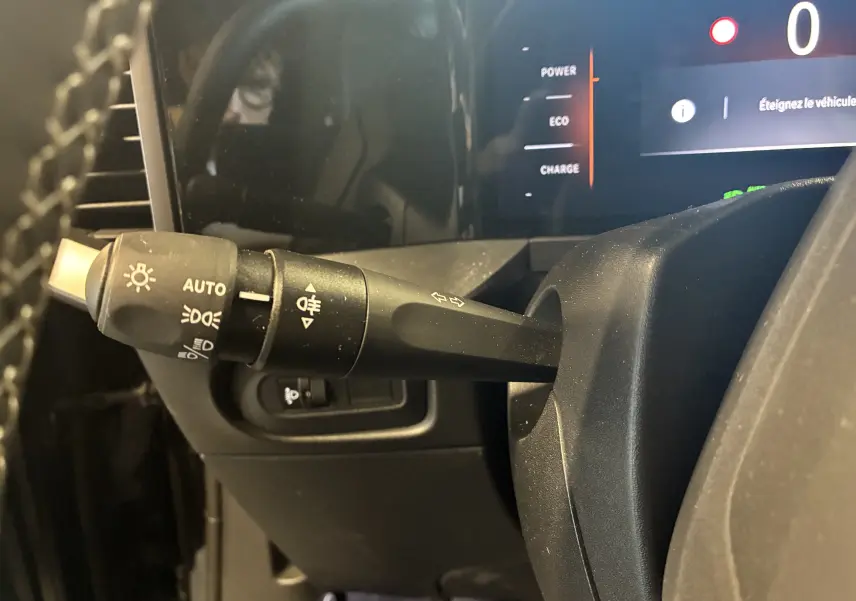 Gros plan sur la manette de clignotants et phares à gauche du volant dans l’habitacle noir de l’Opel Mokka 2025 hybride.