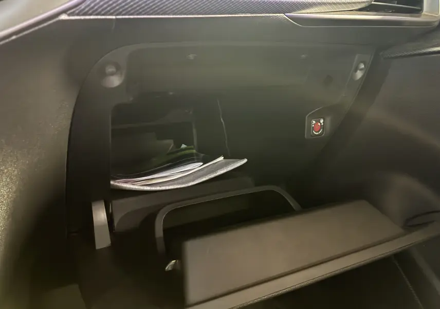 Vue intérieure du vide-poche passager ouvert de l'Opel Mokka 2025 noir, montrant des documents et un bouton rouge distinctif.