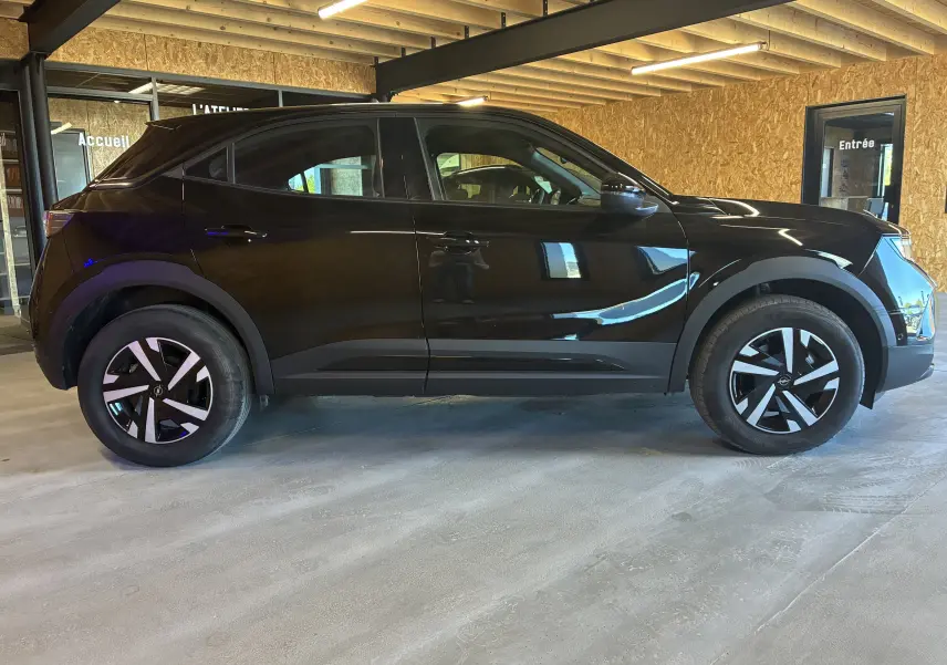 Vue de profil côté gauche d’un Opel Mokka noir 2025 hybride essence, avec jantes noires et détails modernes.