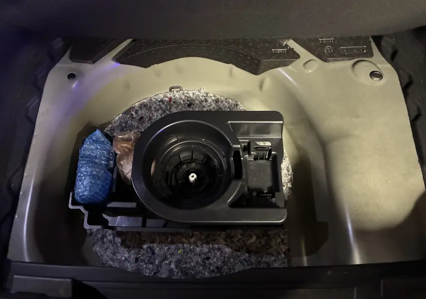 Vue plongeante sur le compartiment de roue de secours d’un Opel Mokka noir 2025, avec support plastique et accessoires.