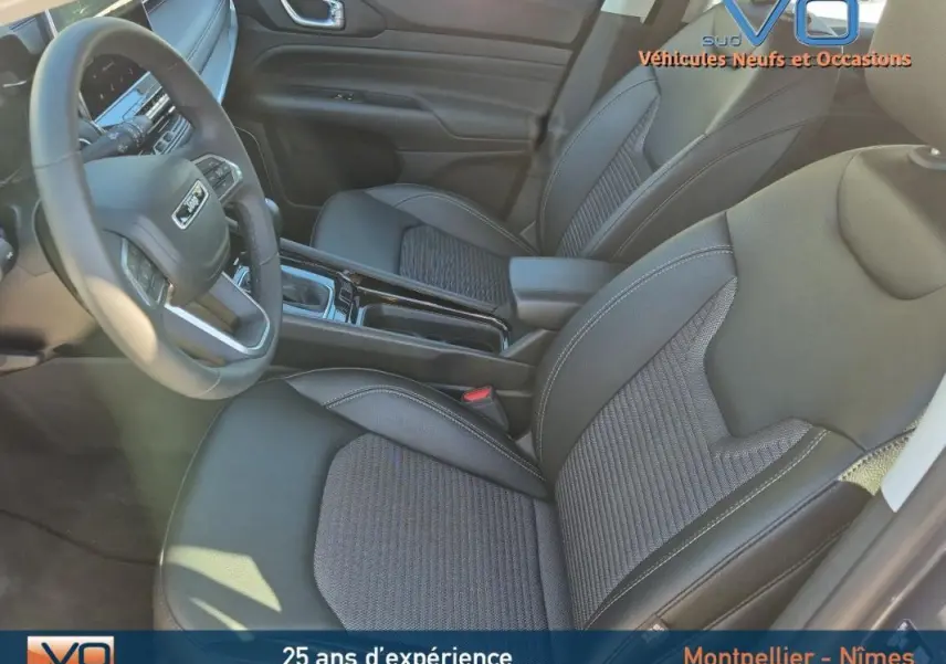Vue intérieure côté conducteur du Jeep Compass 2024 gris, montrant sièges en tissu et cuir avec accoudoir central.