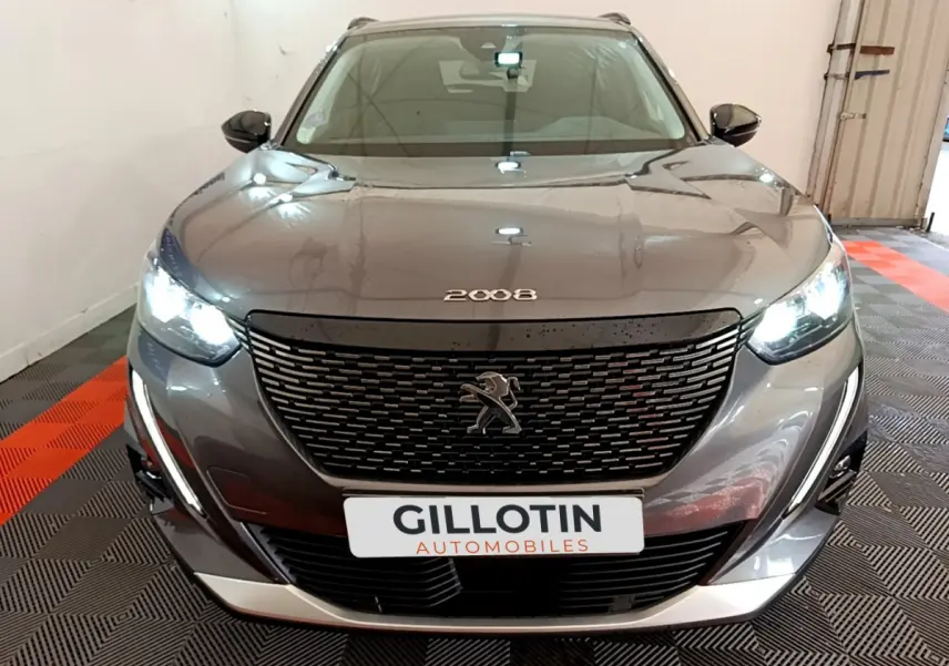 Vue avant d'un Peugeot 2008 gris foncé avec calandre noire et phares LED allumés en intérieur showroom.