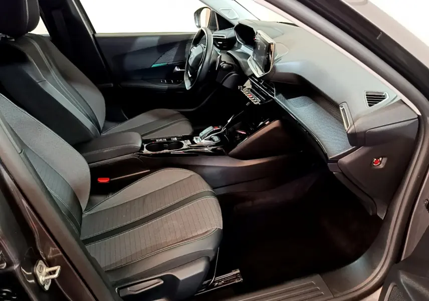 Intérieur vue côté passager du Peugeot 2008 gris foncé, avec tableau de bord moderne et sièges tissu noirs.