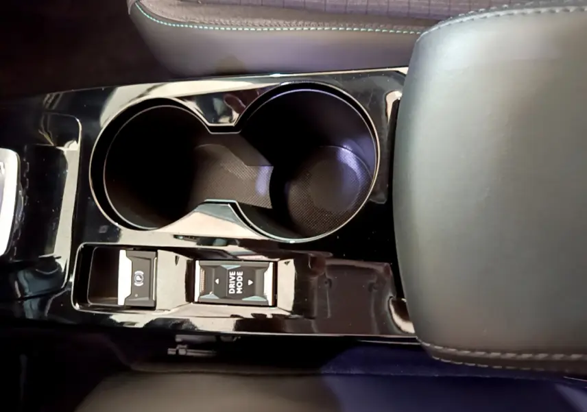 Gros plan sur la console centrale noire brillante du Peugeot 2008 gris foncé, avec porte-gobelets et boutons Drive Mode et frein électrique.