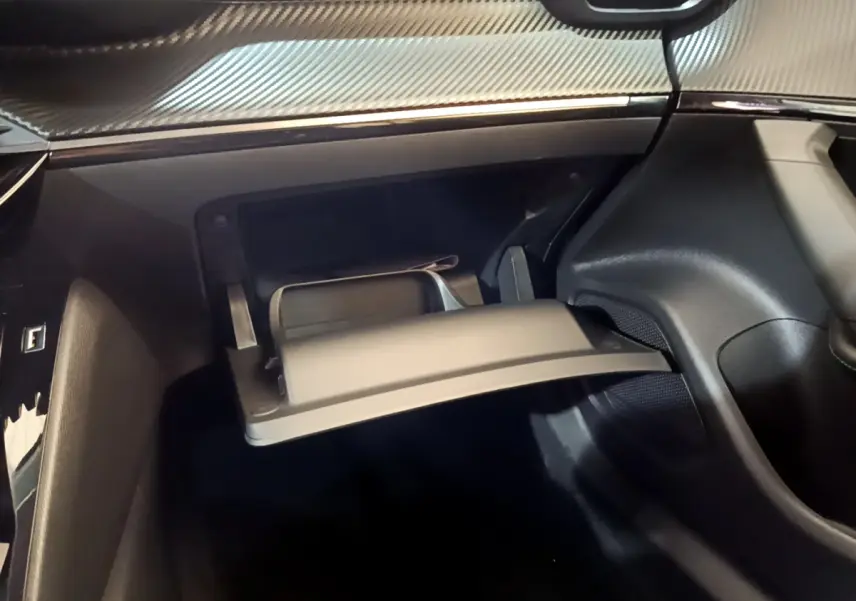 Gros plan sur la boîte à gants ouverte du Peugeot 2008 gris foncé, avec tableau de bord à finition carbone visible.