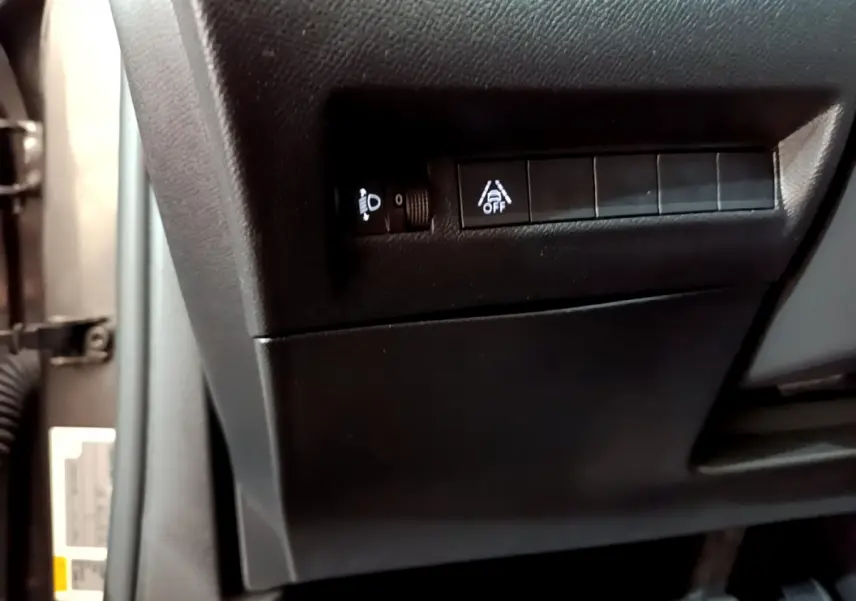 Gros plan sur les commandes de réglage des phares et d'alerte de franchissement de ligne à gauche du volant dans un Peugeot 2008 gris foncé 2022.