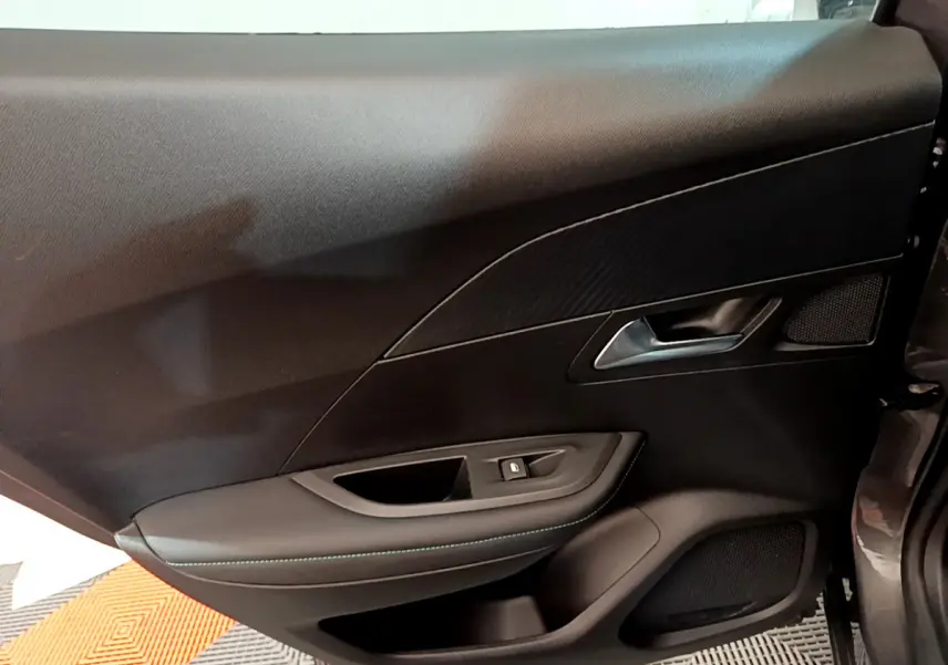 Intérieur côté gauche de la porte d'une Peugeot 2008 gris foncé, avec poignée argentée et garniture noire élégante.