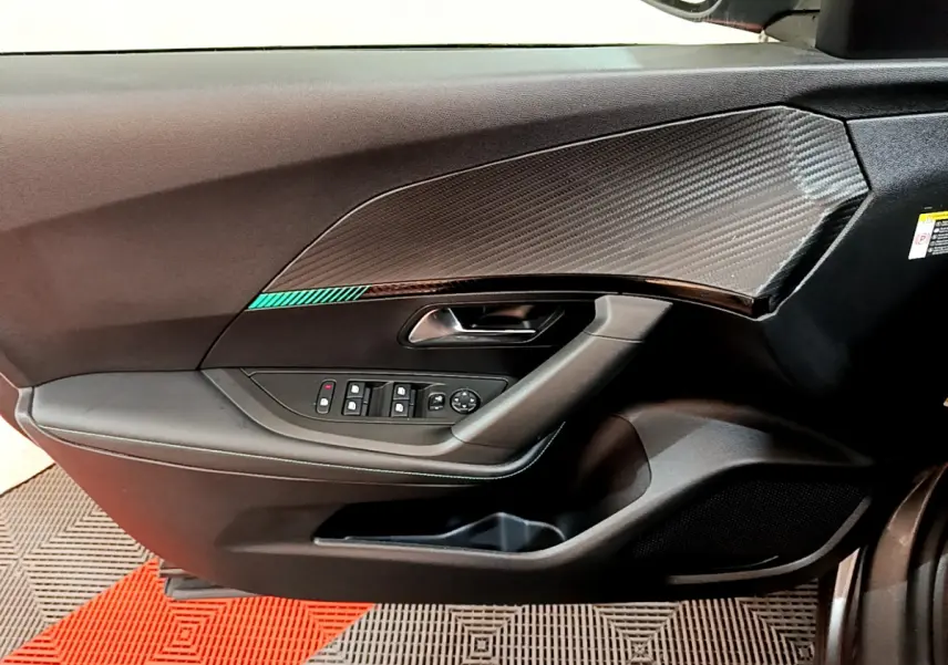 Vue rapprochée de la porte avant gauche du Peugeot 2008 gris foncé avec garniture effet carbone et commandes électriques.