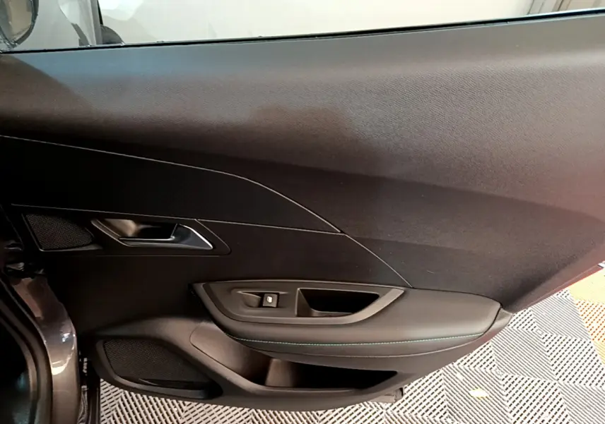 Détail de la porte côté gauche intérieure du Peugeot 2008 gris foncé, avec commandes de vitre et poignée intégrée.