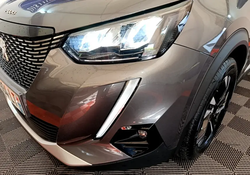 Gros plan sur l'avant droit d'un Peugeot 2008 gris foncé avec phares LED allumés et calandre distinctive.
