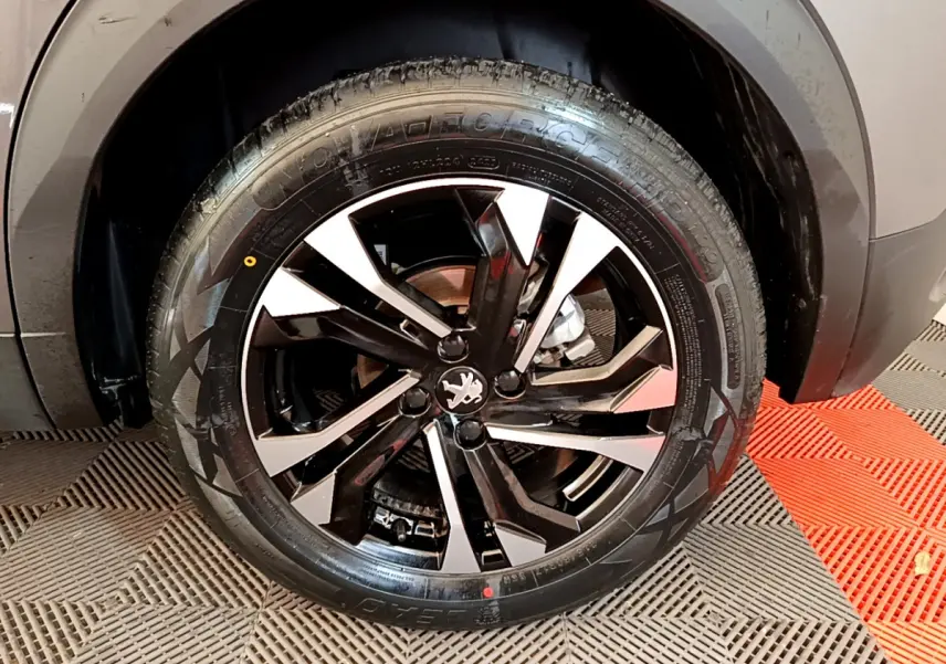 Gros plan sur la roue avant droite du Peugeot 2008 gris foncé, mettant en valeur la jante alliage noire et argentée.