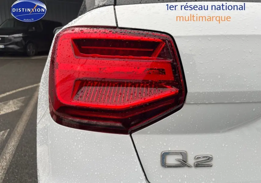 Gros plan sur le feu arrière gauche d’un Audi Q2 blanc Ibis avec logo Q2 sous la pluie.