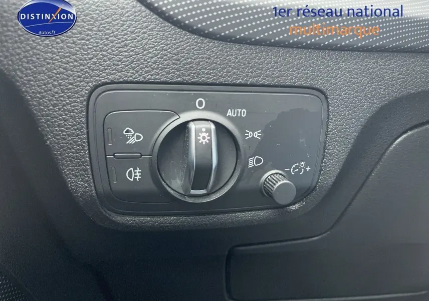 Commande des phares en gros plan sur le tableau de bord noir d’un Audi Q2 blanc, avec réglage automatique et antibrouillard.