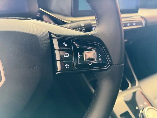 Gros plan sur les commandes du volant en cuir microfibre noir du MG3 Cosmic Silver, avec tableau de bord et écran tactile en arrière-plan.